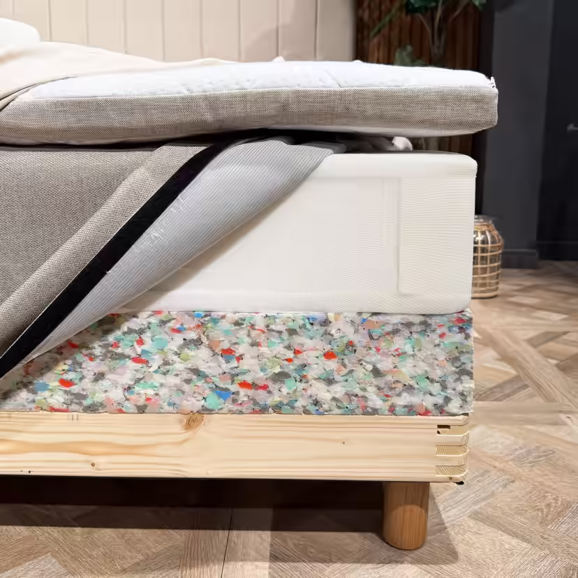 An der Bettecke freigelegte Schichten: Topper, Federkernmatratze mit geöffnetem Bezug und Schaumstoffkante des Bettunterbaus über dem Holzrahmen
